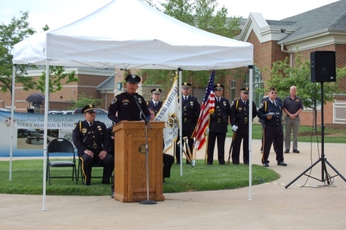 An officer speaks at a podium during the memorial service while the honor guard stands behind him